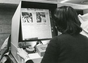 A library patron reads the New York Times on a microfilm reader.