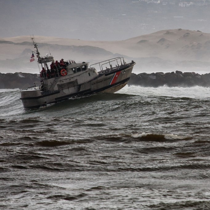 A small coast guard ship moves through large ocean waves.