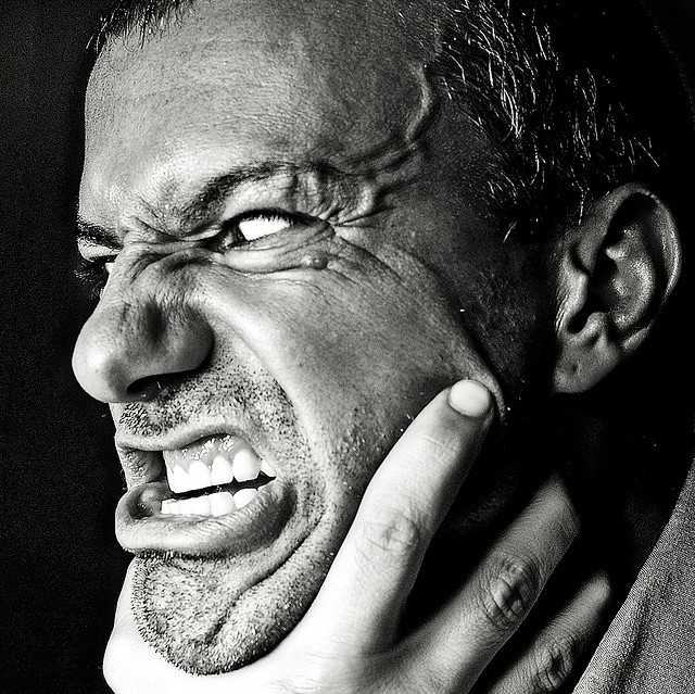 A man with an enraged look on his face and bulging veins on his forehead strains against a hand that is choking him.