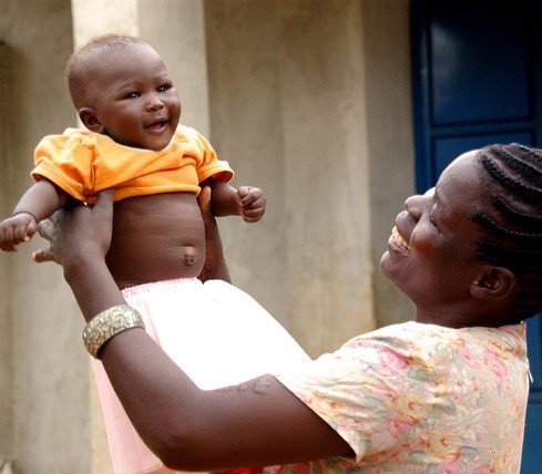 A mother playfully lifts her baby above her head to the baby's delight.