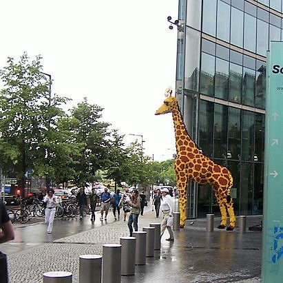 A life-sized model of a giraffe stands in a busy public plaza.